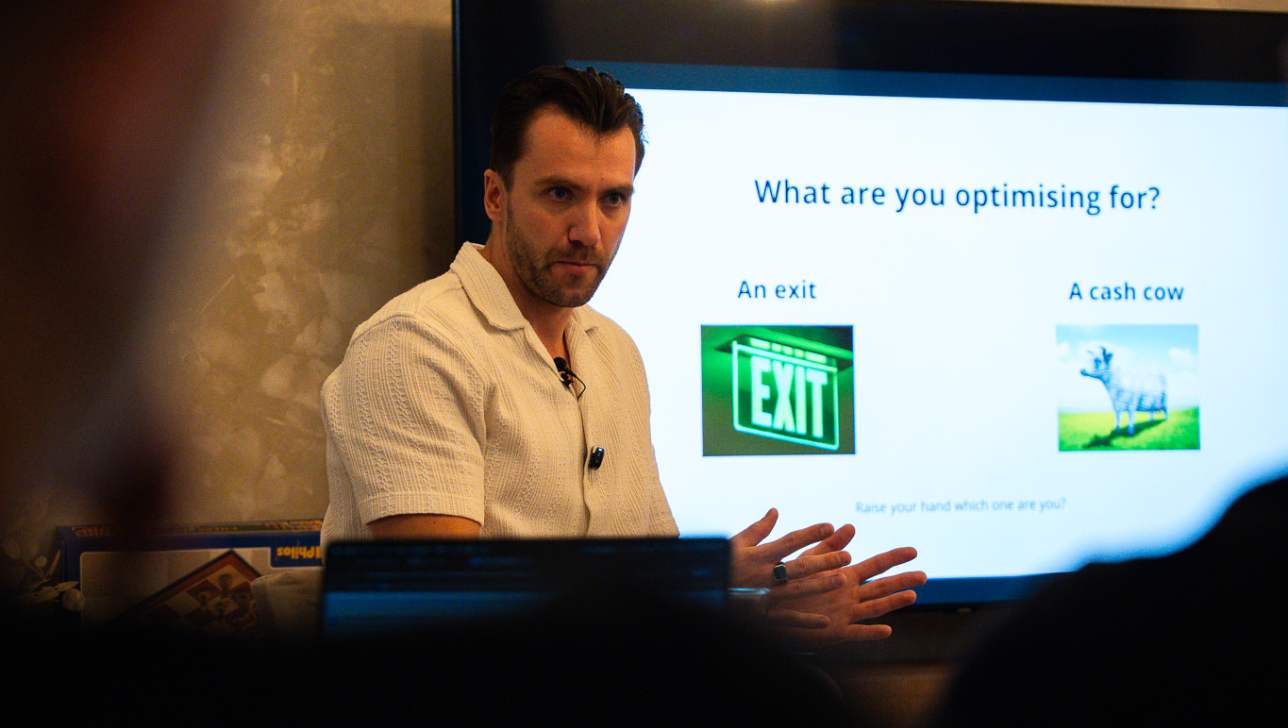 Romans Ivanovs at a BGG Agency Mastermind session, with the slide 'What are you optimising for?' behind him
